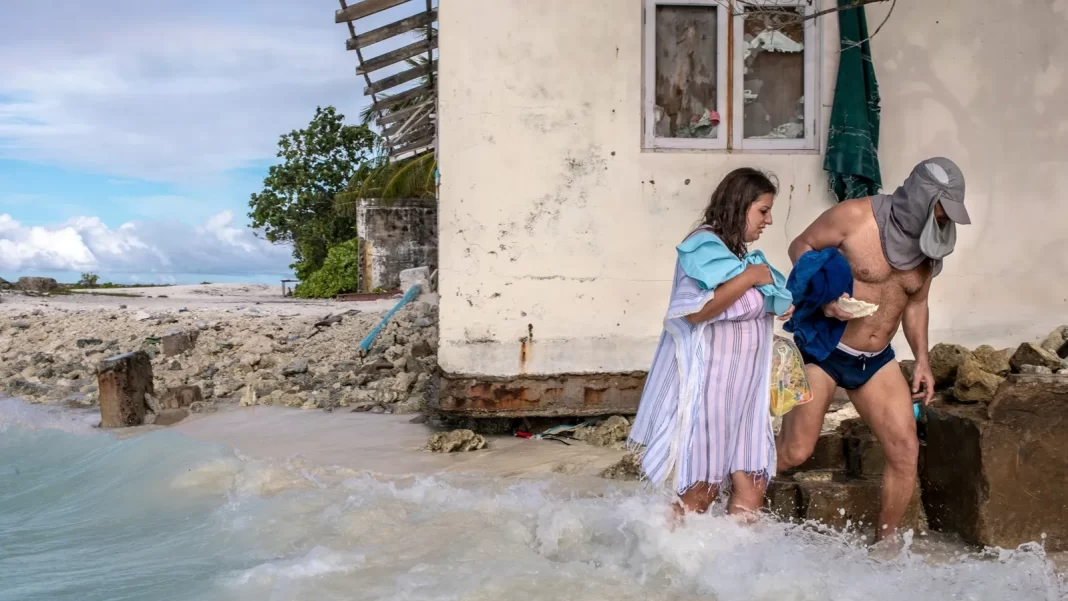 Una pareja camina por el agua, bordeando una casa abandonada en las Maldivas, cuyos cimientos sufrieron una gran erosión debido al aumento del nivel del mar. Van camino a Bikini Beach, donde se permite el uso de bikinis. Fotografía de Marcos Zorzanello. National Geografic.