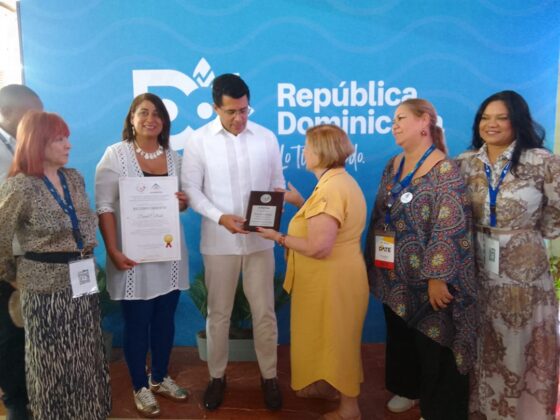 El ministro de Turismo, David Collado recibe un reconocimiento en nombre de Adompretur y FIPETUR de manos de Yenny Polanco Lovera y María Shaw.