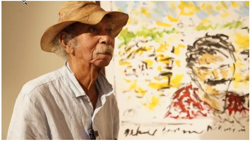 El maestro José Cestero junto a uno de los cuadros de la exposición Macondo en Santo Domingo, en el que resalta la imagen del escritor Gabriel García Márquez.