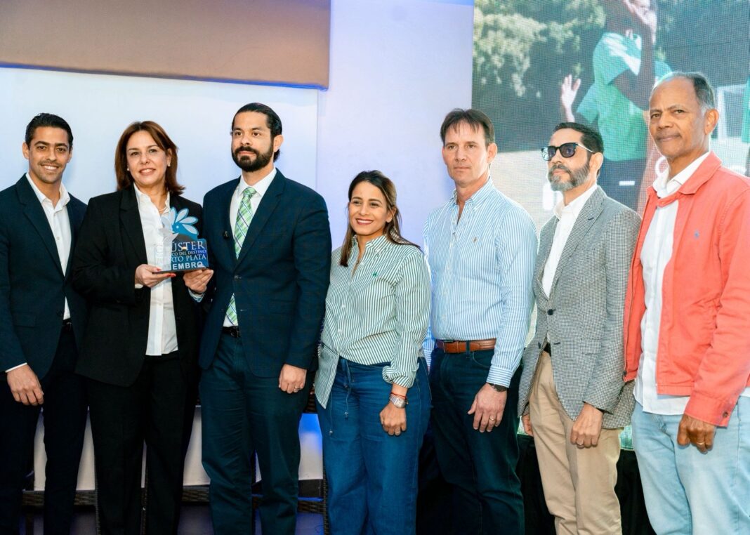 Birgitt Heinsen, presidente del Clúster Turístico del Destino Puerto Plata y Yerik Pérez, presidente de ADOTURD, sostienen una placa del clúster al momento de la firma del acuerdo.
