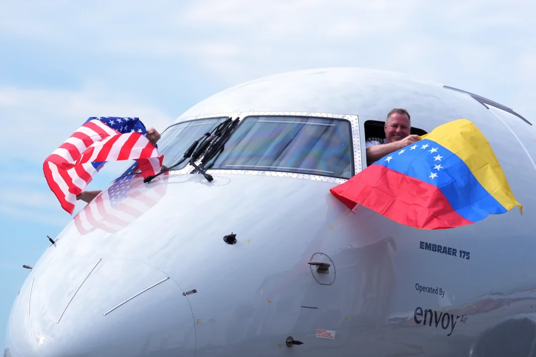 El capitán Ric Wilson ondea una bandera venezolana y el primer oficial saluda a la bandera estadounidense mientras se preparan para volar en el vuelo AA3599 de American Airlines, el primer vuelo comercial directo entre Estados Unidos y Venezuela en siete años, el jueves 30 de abril de 2026, en el Aeropuerto Internacional de Miami. (Foro de la agencia AP de Rebecca Blackwell)